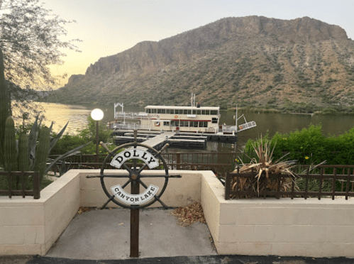 A scenic view of Canyon Lake with a boat docked, framed by a decorative sign and surrounding greenery.